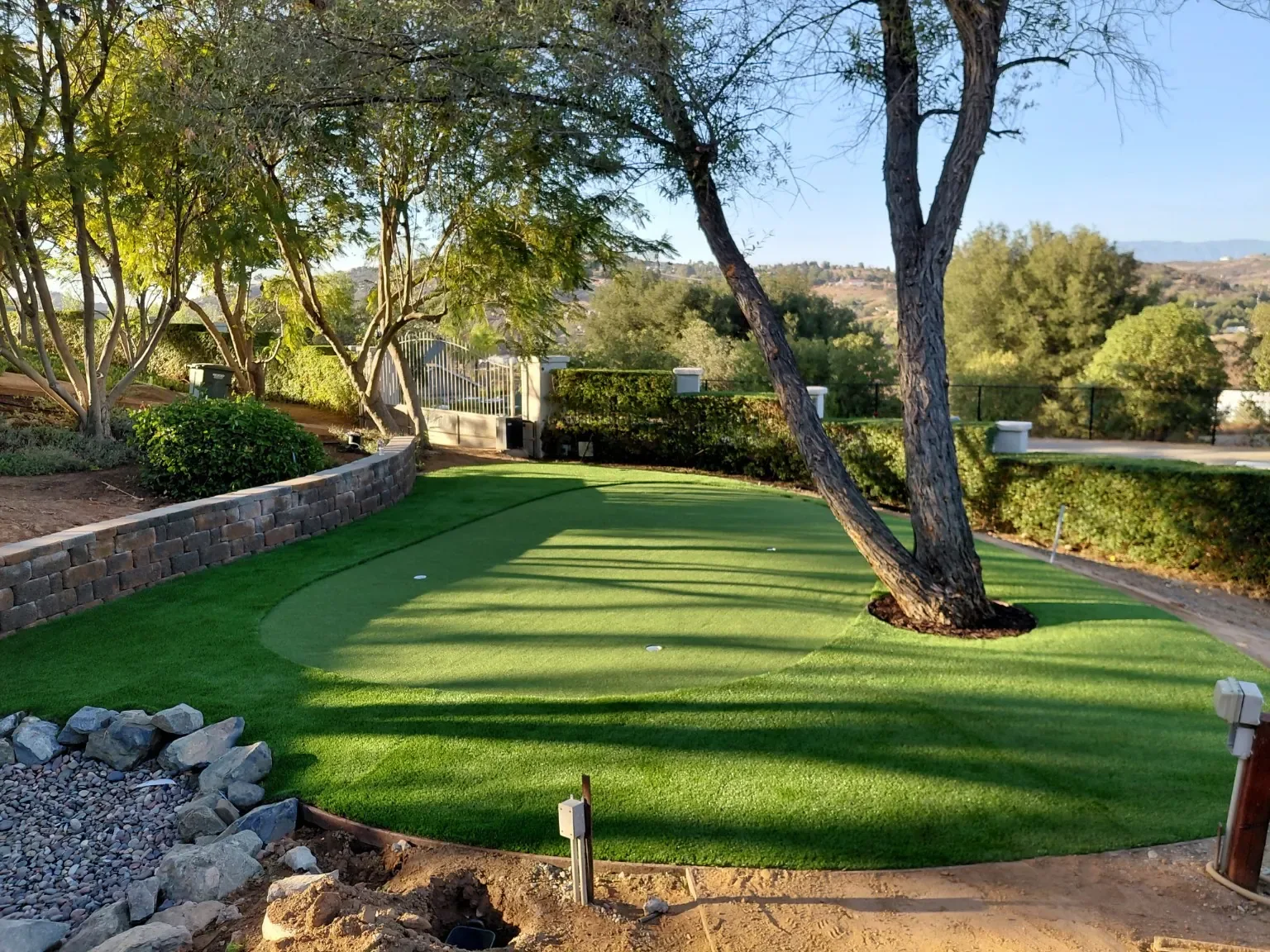 A landscaped backyard with a green putting area, mature trees, and stone borders
